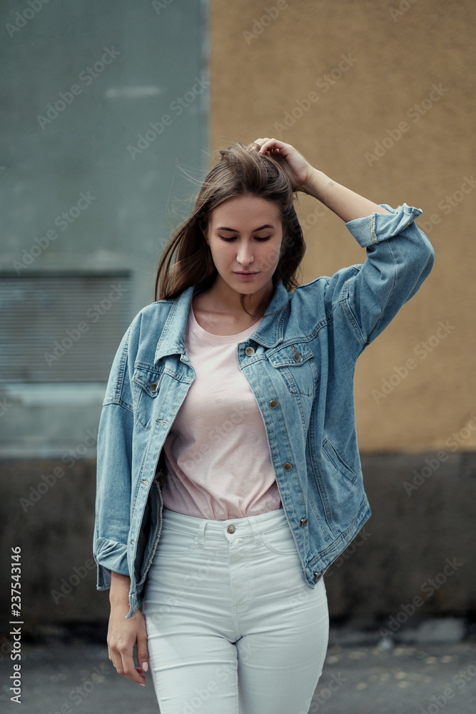 Young beautiful girl with long hair in a T-shirt and denim jacket on the background of vintage concrete wall. Young beautiful girl with long hair in a T-shirt and denim jacket on the background of vintage concrete wall.