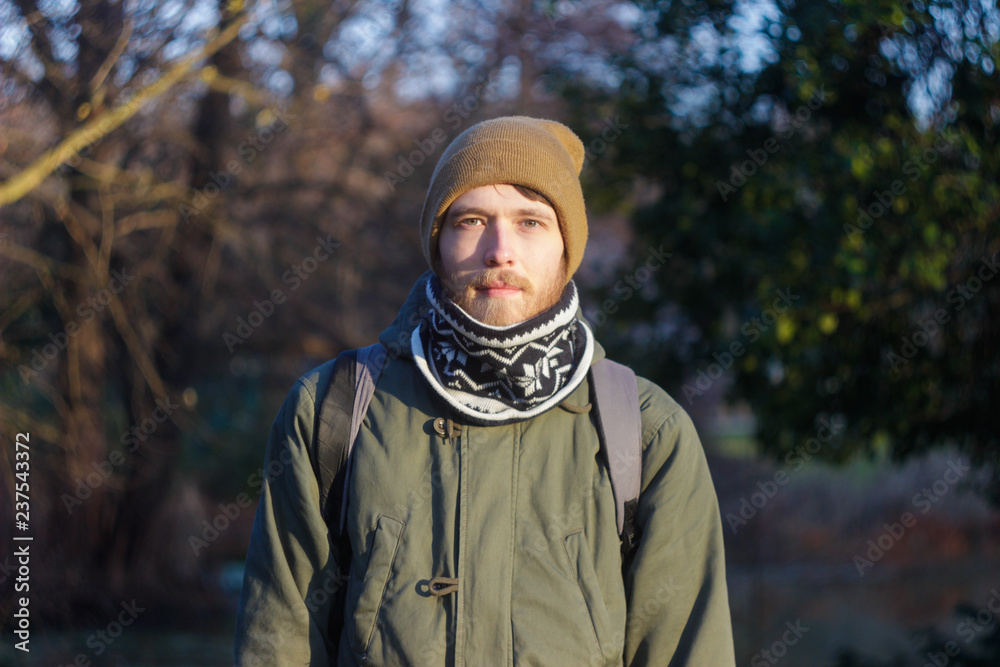 Young blond white man with a beard wearing a scarf, hat and backpack walking through the woods Young blond white man with a beard wearing a scarf, hat and backpack walking through the woods