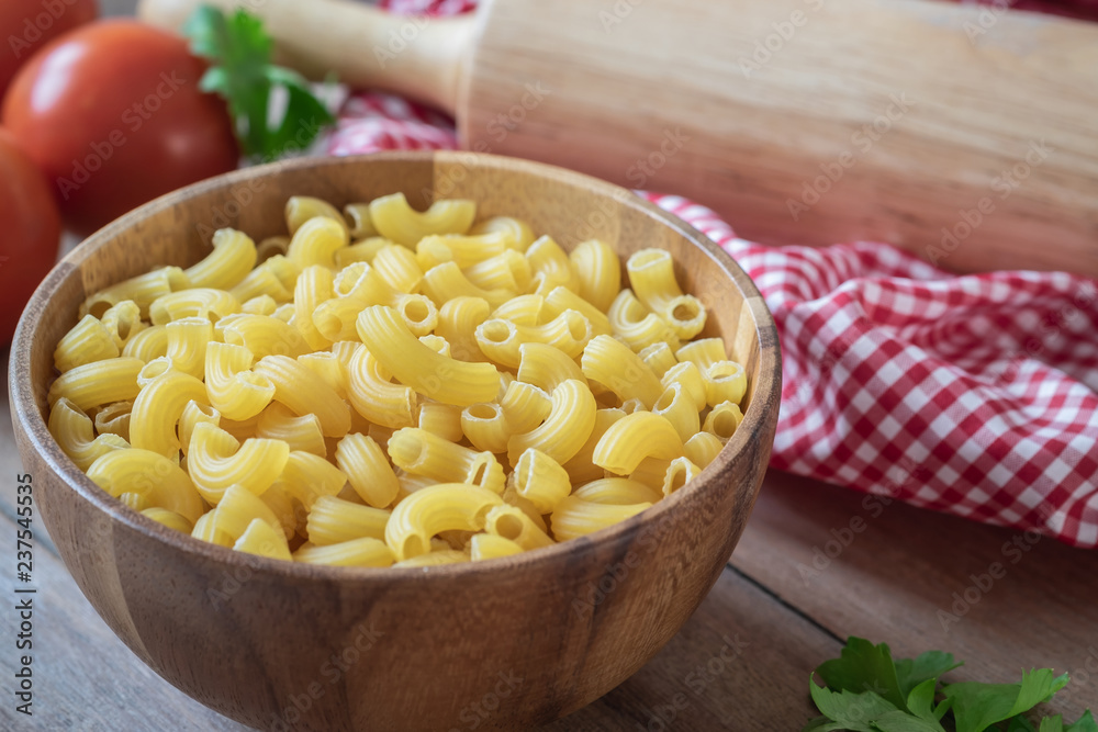 Raw macaroni pasta in wooden bowl