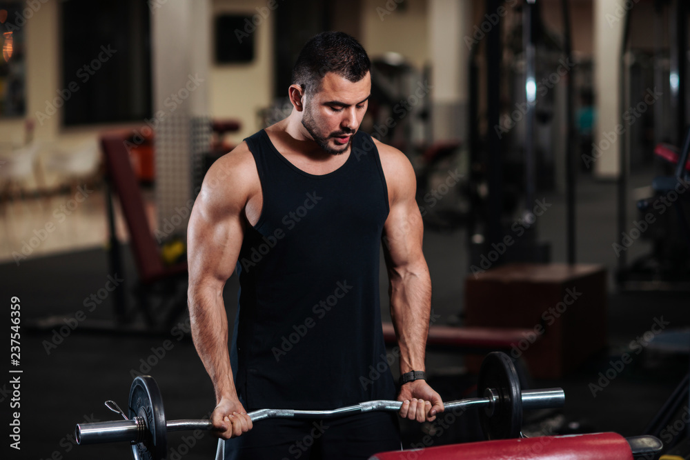 Man trains biceps in the gym. Muscular bodybuilder guy doing exercises with a barbell. Man trains biceps in the gym. Muscular bodybuilder guy doing exercises with a barbell.