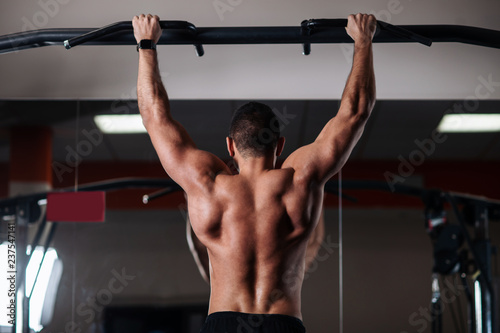 Athletic man making pull-up exercises on a crossbar in the gym