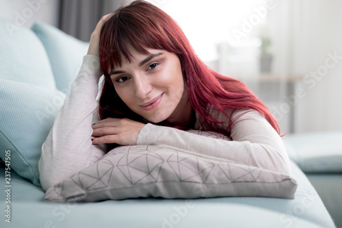 Woman with friendly smile looking at camera while lying on sofa in living room