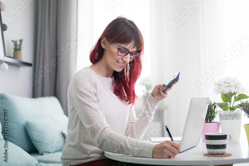 Woman at home using laptop and calculator checking bills and invoice document