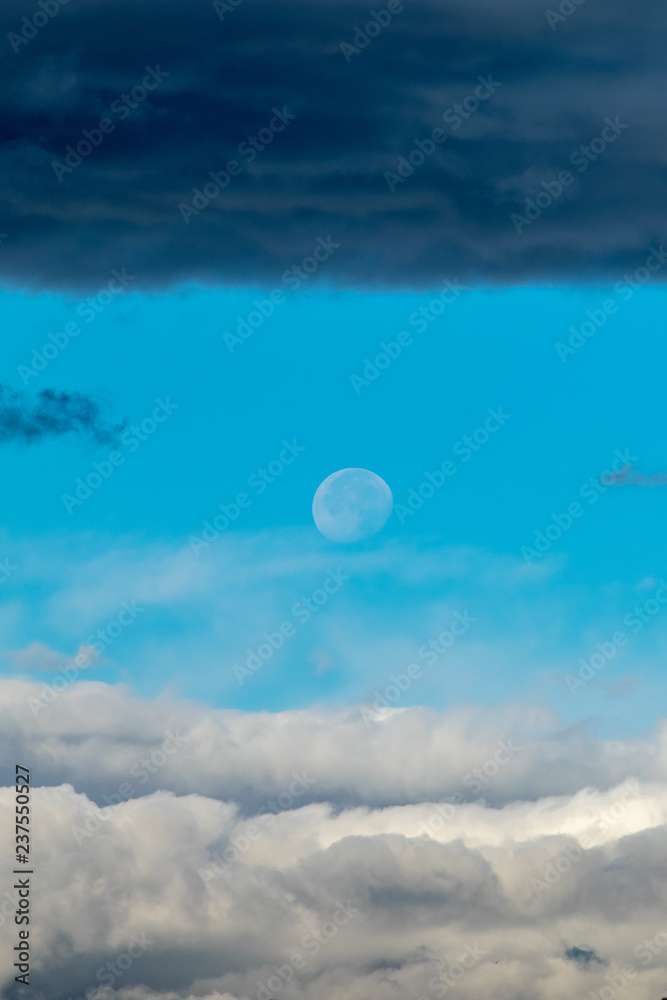an interesting shot of the moon out during the day caught between two different colour clouds taken from Marbella, Spain 