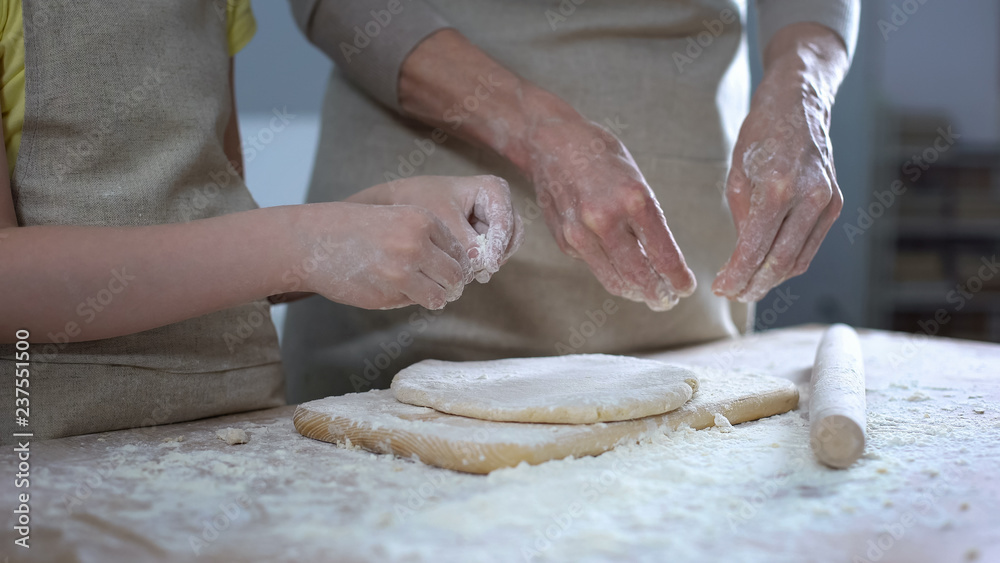Female kid helping grandmother to roll dough for pizza, family recipe, cooking