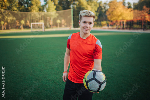 Cheerful and attractive young player hold ball in hand. He offers it. Guy smiles. He stand on lawn. photo