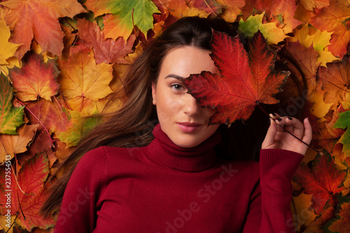 Girl holding red maple leaf in hand over colorful fallen leaves background. Sunny day, warm weather. Gold cozy autumn concept. Top view. Copy space