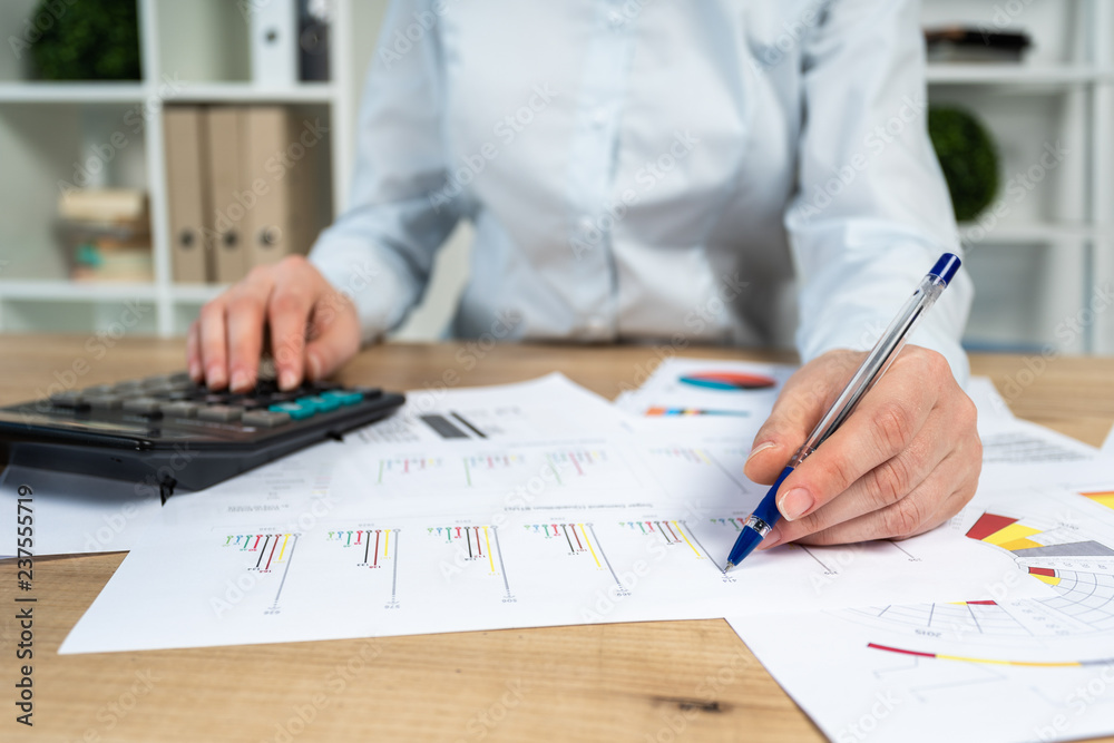 Cropped close up photo of lady in her formalwear she sit behind table with charts graph diagram in bright loft interior mark important spot on graphics by pen focus on hand Cropped close up photo of lady in her formalwear she sit behind table with charts graph diagram in bright loft interior mark important spot on graphics by pen focus on hand