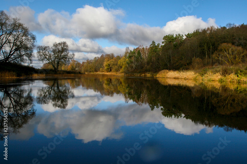 Autumn landscape with colorful trees, yellow grass and river. Reflection in river © Roberts Ratuts