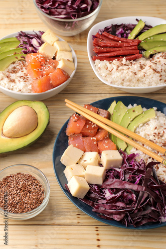 poke bowl Hawaiian food. a plate of rice, salmon, avocado, cabbage and cheese. next to sesame and fresh avocado on a natural wooden table