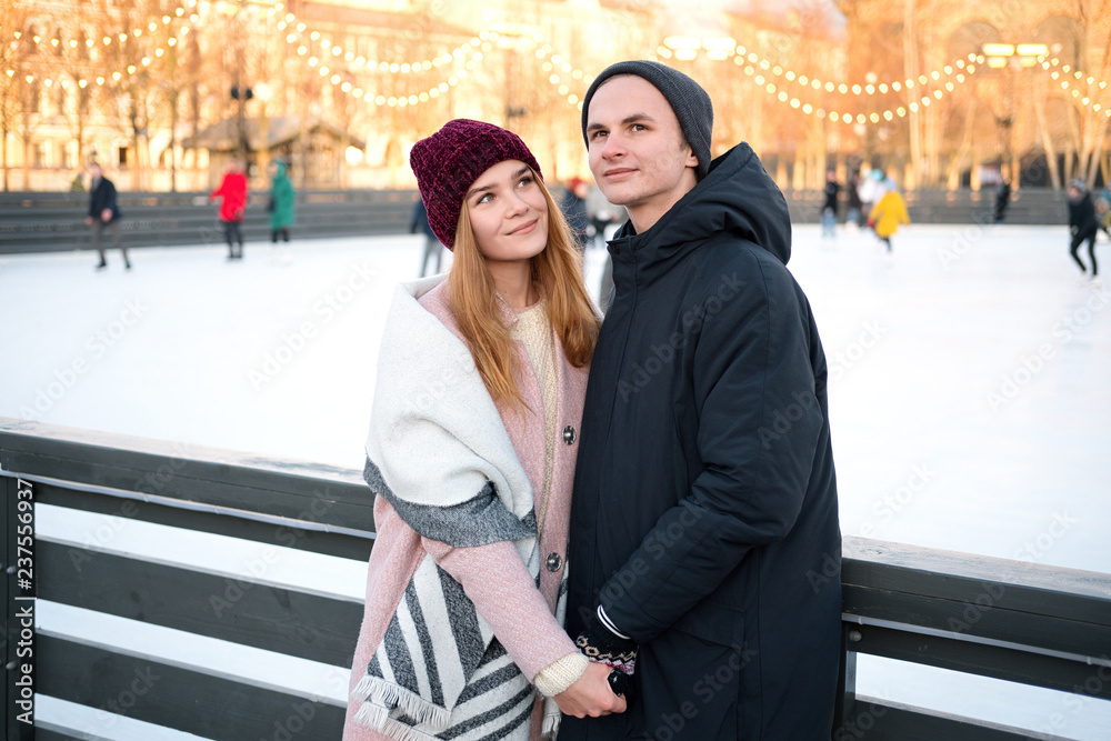 Young romantic carefree couple in love holding hands enjoying romantic moment together outdoors near ice rink in winter.