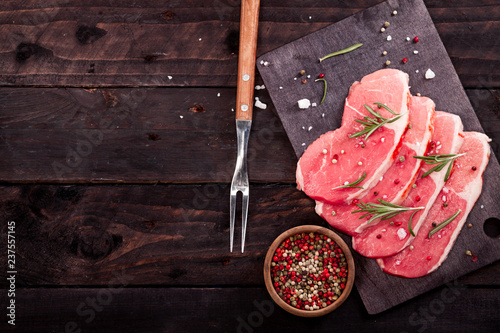 Raw beef steak on a cutting board with rosemary and spices.