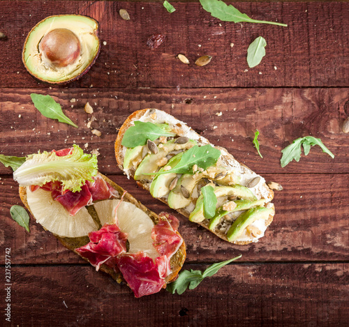 Bruschettas with cheese, avocado, rucola, nuts, prosciutto, pineapple on wooden table