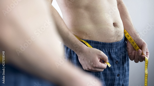 Canvas Print Man in home clothes measuring volume of his hips after debilitating diet