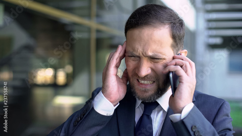 Overworked male manager talking on phone, suffering from migraine, headache