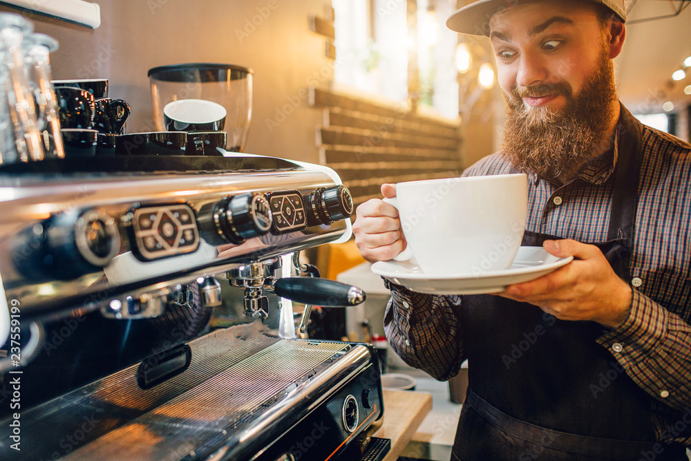 Excited and strange looking barista holding huge white cup of coffee in  hands. He looks at it. Guy stand in kitchen at coffee machine. Stock-Foto |  Adobe Stock