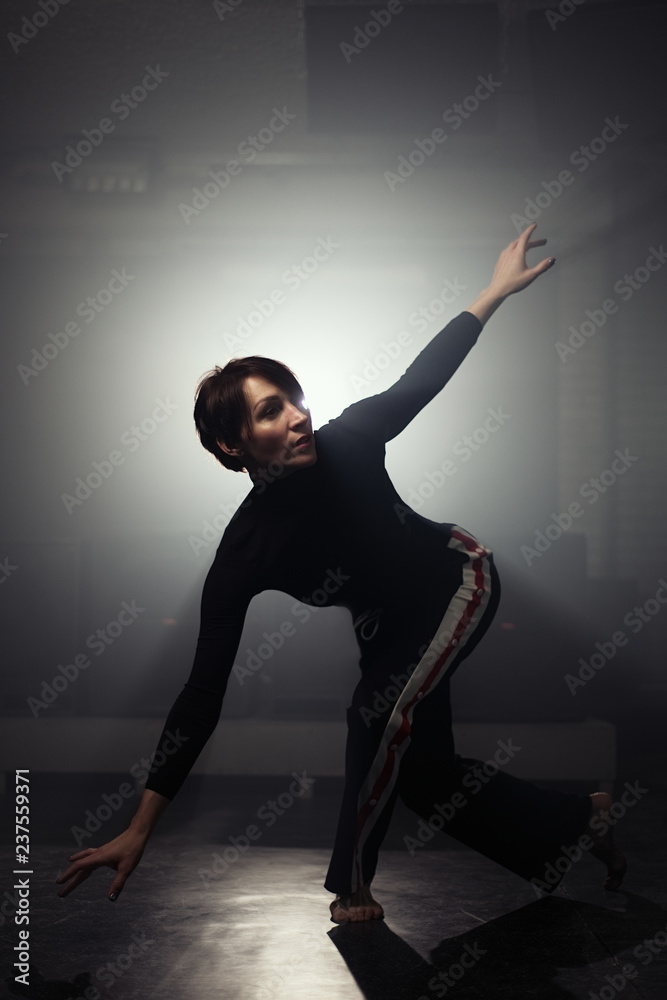 Obraz premium modern beautiful dancer in black clothes posing against the Studio in the smoke