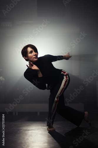 modern beautiful dancer in black clothes posing against the Studio in the smoke