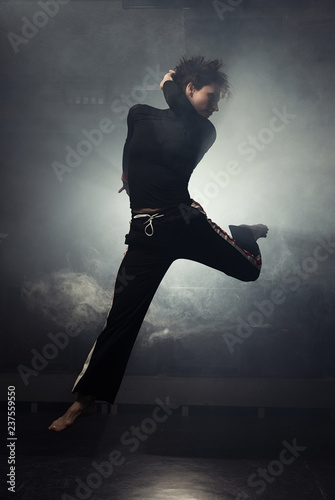 modern beautiful dancer in black clothes posing against the Studio in the smoke