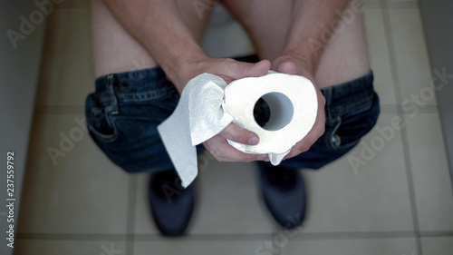 Man holding toilet paper roll, feeling hemorrhoid pain, bowel disease, health