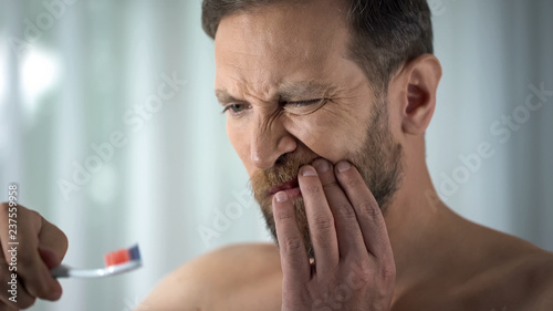 Caucasian man brushing teeth and seeing blood on toothbrush, dental care, ache photo
