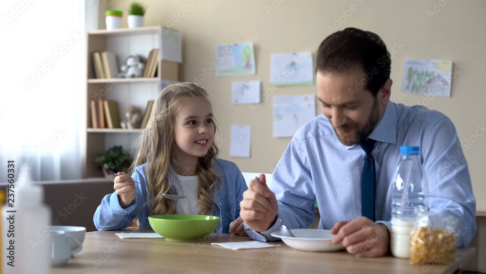 Caring father and little daughter eating cornflakes and talking, morning ritual