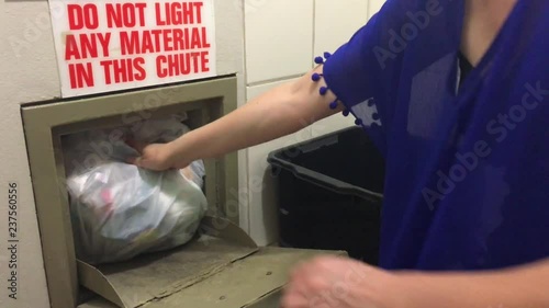 Woman throwing away a garbage packed in a garbage bag using a home garbage chute in dwelling house.