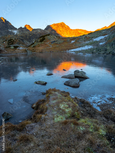 Vertical photograph of a morning in high mountains with a frozen lake in the front