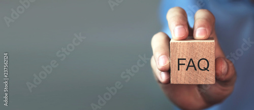 Man holding FAQ message on wooden cube. Frequently Asked Questions photo