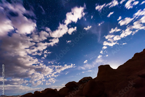 Night sky with full moon rising  or moonrise  in Goblin Valley State Park in Utah showing clouds  stars  and canyons silhouettes in wilderness nature