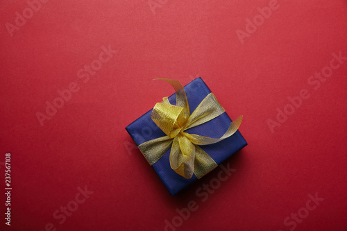 Top view of wrapped gift with golden ribbon on red background