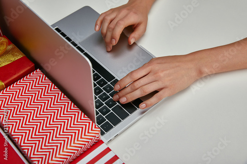 Cropped view of woman typing on laptop near wrapped gifts