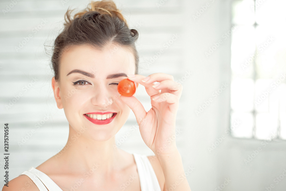 Young smiling woman tasting fresh organic cherry tomato sits in a white bright room. Healthy lifestyle concept. Young smiling woman tasting fresh organic cherry tomato sits in a white bright room. Healthy lifestyle concept.