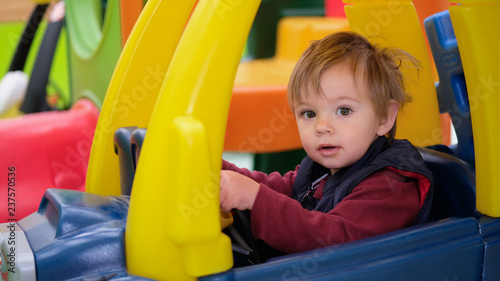 Toddler boy driving a sit and ride car.