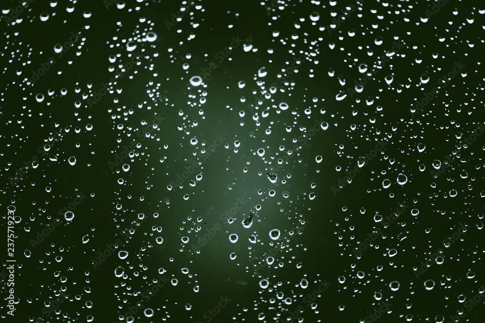 Obraz premium Dirty window glass with drops of rain. Atmospheric green background with raindrops. Droplets and stains close up. Detailed transparent texture in macro with copy space. Rainy weather.