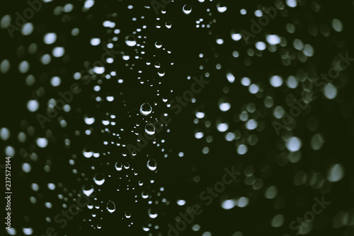 Dirty window glass with drops of rain. Atmospheric green background with raindrops in bokeh. Droplets and stains close up. Detailed transparent texture in macro with copy space. Rainy weather.