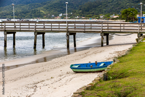 Detail of wooden pier of Morrinhos beach, with wooden fishing boat and Zimbros beach in the background, Bombinhas, Santa Catarina photo