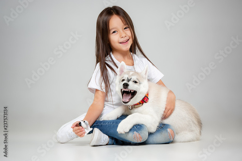 Portrait of a joyful little girl having fun with siberian husky puppy on the floor at studio. The animal, friendship, love, pet, childhood, happiness, dog, lifestyle concept