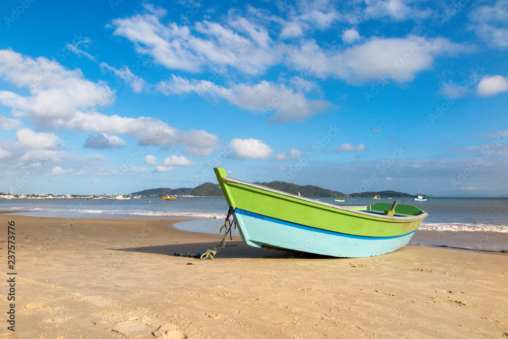 Fishing boat on the sand of Zimbros beach at dusk, calm sea and blue sky with clouds, Bombinhas, Santa Catarina