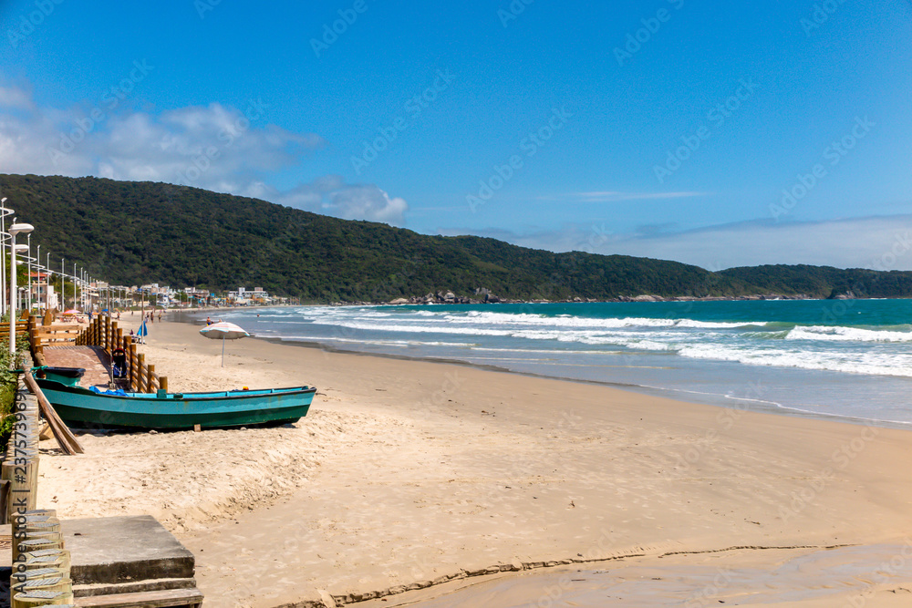 Left side of Bombas beach, with calm sea and hill in the background, blue sky with few clouds, Bombinhas, Santa Catarina