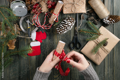 Christmas workshop theme. Top view of woman hands wrapping New Year present and tie bow.