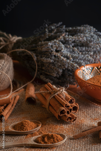 Ground cinnamon, cinnamon sticks, tied with jute rope on old straw bag background in rustic style