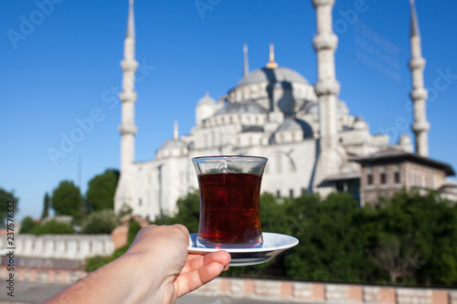 Woman holding cup of traditional Turkish tea on terrace with view of the Blue Mosque in Istanbul in Turkey.