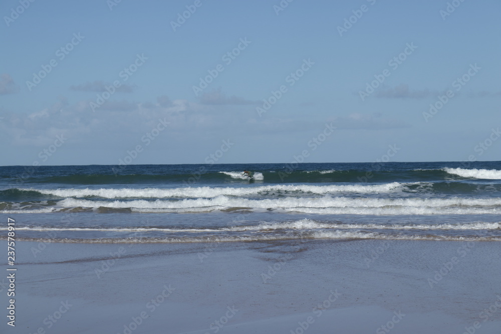 surfer in the background in the middle of the waves on the beach