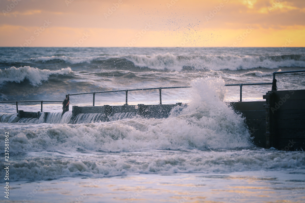 Crashing wave against a jetty during a stormy sunset in Criccieth, Wales, UK