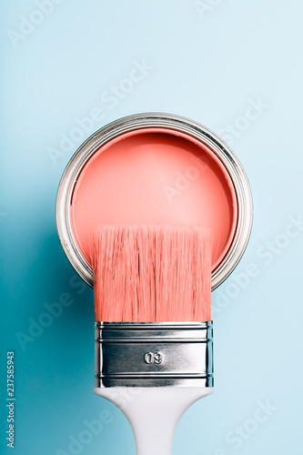 Brush with white handle on open can of Living Coral paint on blue pastel background. Color of the year 2019. Main trend concept.