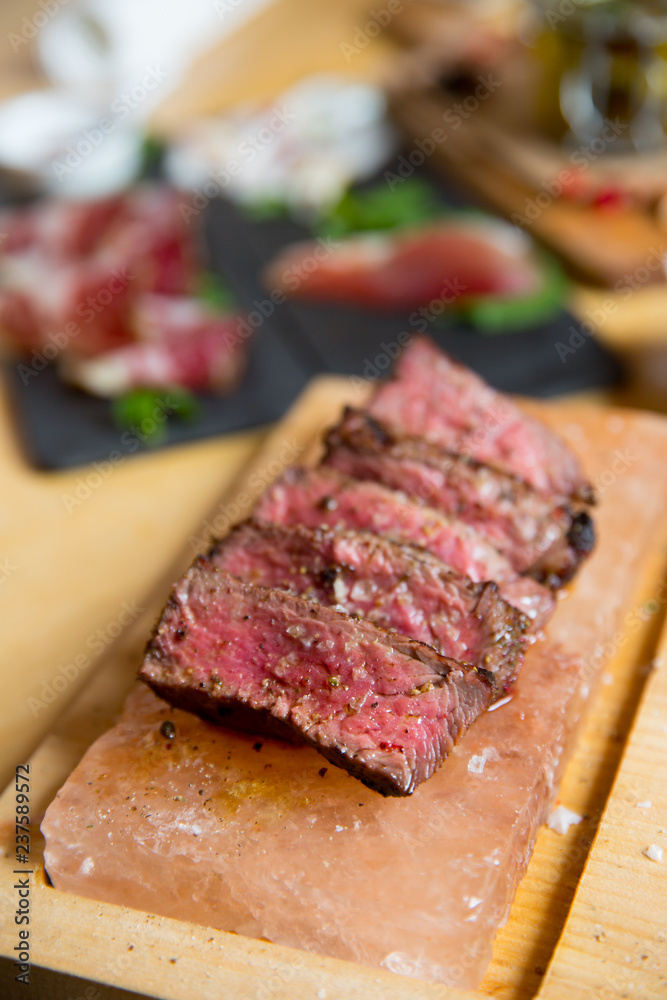 Juicy medium Beef Rib Eye steak slices in pan on Himalayan pink salt plates.