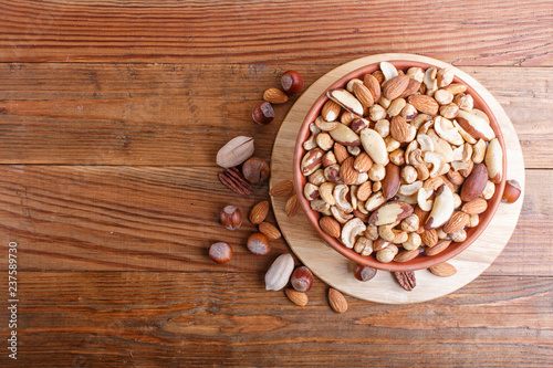 Mixed different kinds of nuts in ceramic bowl on brown wooden background with copy space.
