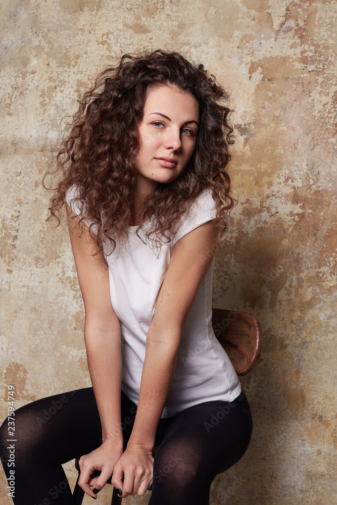 Young cute blue eyed seductive curly haired female posing for new season fashionable collection of women’s underwear, dressed in black tights and casual white cotton t-shirt. Advertisement concept.