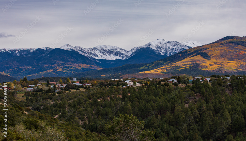 Small town at the foot of mountains with snow cap tops and autumn forest